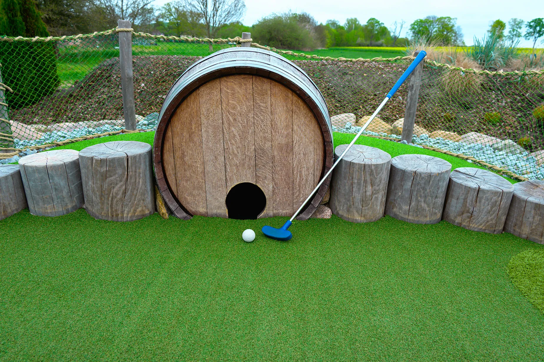 A miniature golf course with a wooden barrel.