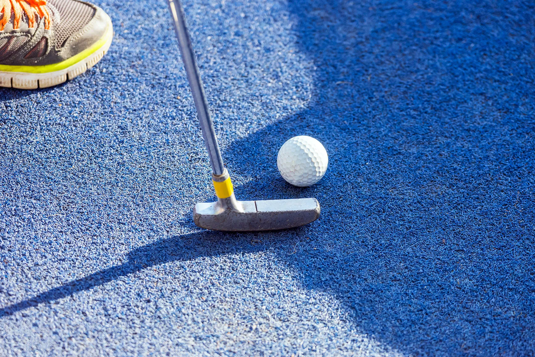 A golf ball and a putter on a blue carpet.