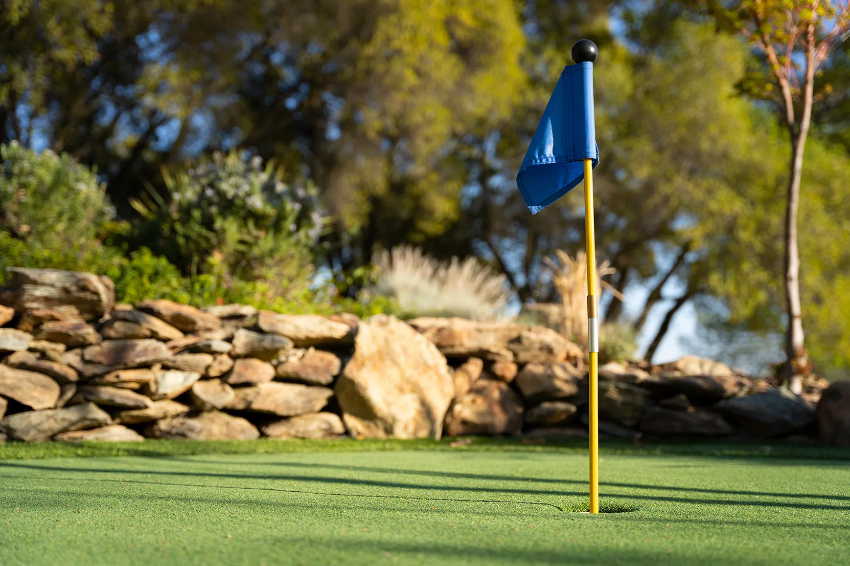 A blue flag on a golf course with a stone wall in the background.