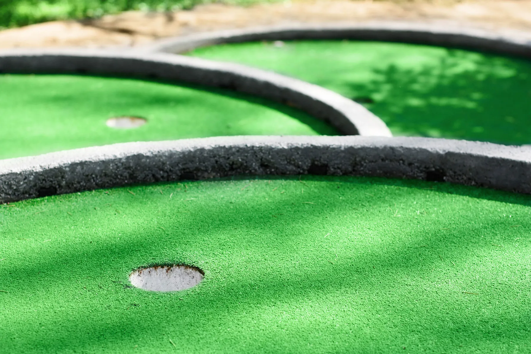 A close up of a green golf course with a hole in the middle.
